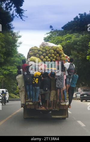 Cagayan de Oro, Philippinen: Die Menschen hängen an der Rückseite eines beweglichen Jeepneys, der mit Obst, Sacksäcken mit Gemüse und Kisten mit Bier gefüllt ist. Öffentliche Verkehrsmittel. Stockfoto