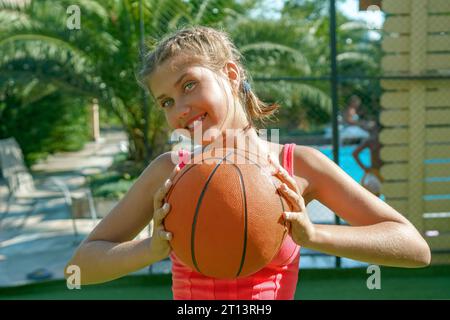 Ein fröhliches, attraktives Teenager-Mädchen hält einen Basketball in den Händen. Stockfoto