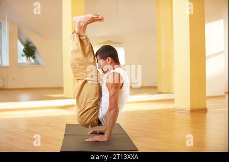 Ein junger starker Mann, der handstehende Yoga-Übungen macht - Urdhva Brahmachariasana im Yoga-Studio. Stockfoto