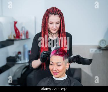 Der Friseur färbt das Haar einer Asiatin in Rosa. Kurzer, extremer Haarschnitt. Stockfoto