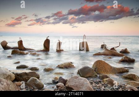 Massive Beton-Tetrapoden bilden einen Wellenbrecher mit weichem, blauem Meer bei Sonnenuntergang Stockfoto