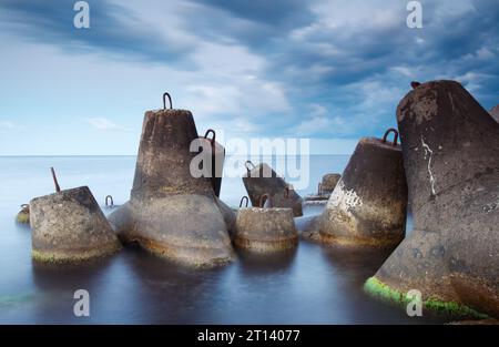 Massive Beton-Tetrapoden bilden einen Wellenbrecher mit weichem, blauem Meer bei Sonnenuntergang Stockfoto