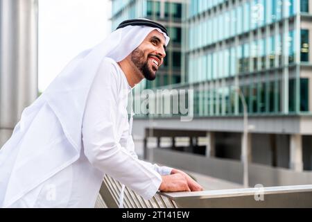 Arabischer Mann aus dem Nahen Osten, der in der Stadt traditionelle emiratische Kandora-Kleidung trägt - arabischer muslimischer Geschäftsmann, der durch das städtische Geschäftszentrum schlendert. Stockfoto