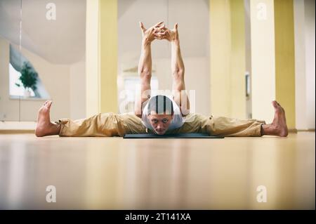 Ein junger starker Mann, der Yoga-Übungen macht - Samakonasana gerade Winkel-Pose im Yoga-Studio. Stockfoto