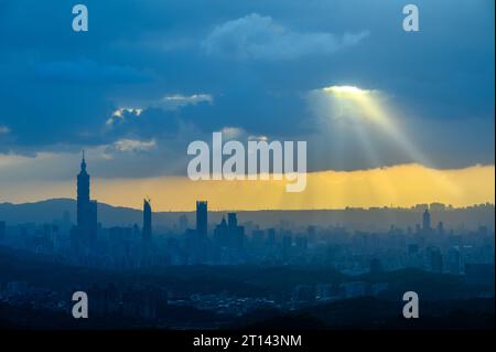 In der Abenddämmerung bricht die Sonne durch die Wolken und scheint auf Taipeh City. Silhouetten von Stadtgebäuden. Orangefarbener Himmel und dunkle Wolken. Stockfoto