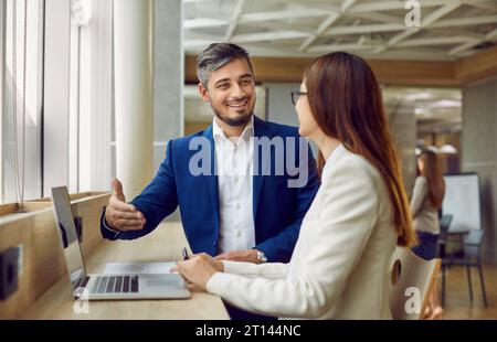 Ein lächelnder männlicher Verkäufer trifft sich mit einer jungen Kundin und bietet ihr gutes Geschäft an Stockfoto
