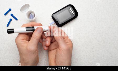 Kaukasischer Mann mittleren Alters hat sich seinen Finger für den Glukosetest zu Hause mit Messgerät und Zubehör im Hintergrund durchbohrt Stockfoto