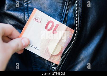 Die Hand zieht Papiergeld und Karte aus der Tasche. Ein Dieb hat einen Mann ausgeraubt. Bargelddiebstahl, kriminelles Konzept. Stockfoto