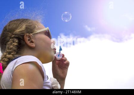 Das Mädchen fängt Seifenblasen an. Das glückliche spielende Kind vor dem Hintergrund des Himmels. Konzeptkindschaft, glückliches Kind Stockfoto