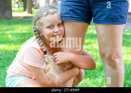 Das Kind umarmt Moms Bein. Porträt eines netten Mädchens, das Mutter hält. Die Liebe des Kindes zu den Eltern. Unglücklicher Teenager. Depressives Mädchen. Düsteres Kind Stockfoto