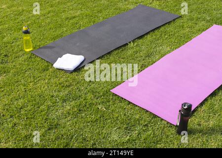 Nahaufnahme von Yogamatten, Handtuch und Wasserflaschen auf Gras im sonnigen Garten, Kopierraum Stockfoto