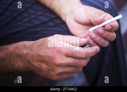 Der Mann hält eine Zigarette und das Feuerzeug in der Hand. Abhängigkeit von einer sucht. Vor dem Rauchen. Raucherkonzept, Raucher. Nahaufnahme Stockfoto