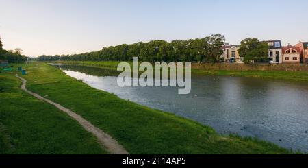 Stadtbild mit Fluss uzh. Ufer der Innenstadt mit alten Gebäuden am anderen Ufer in der Ferne. Sonniger Sommermorgen Stockfoto