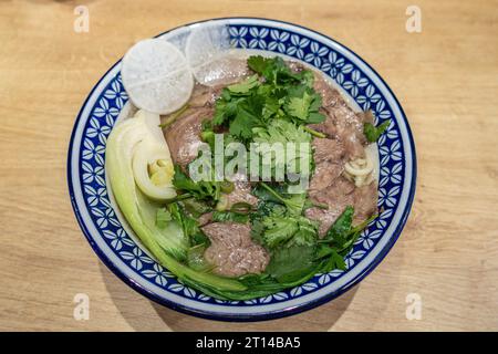 Eine Schüssel asiatischer Nudeln mit Rindfleisch, pak Choi, Rettich in Scheiben in Rinderbrühe zum Mittagessen Stockfoto
