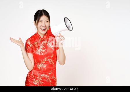 Asiatische Frau trägt traditionelles Cheongsam Qipao Kleid mit Geste, die Megaphon isoliert auf weißem Hintergrund hält. Glückliches chinesisches Neujahr. Stockfoto
