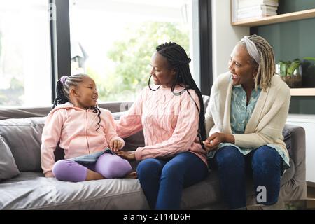 Glückliche afroamerikanische Seniorenmutter, Erwachsene Tochter und Tochter sitzen auf der Couch und reden Stockfoto