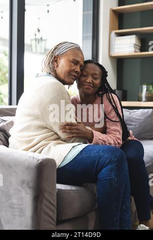 Glückliche afroamerikanische Seniorenmutter und erwachsene Tochter sitzen auf der Couch und umarmen sich Stockfoto