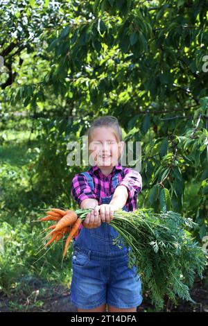 Baby Mädchen hält Karotten im Garten Kind essen gesunde Ernährung Lebensstil vegan Bio-Rohgemüse Home gewachsen Sommer Gartenarbeit Konzept Stockfoto