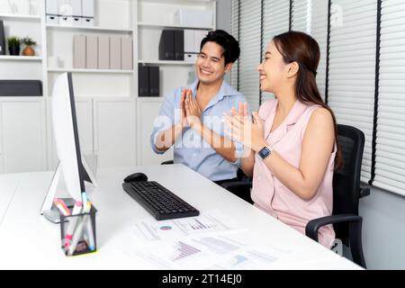 Zwei asiatische Geschäftsleute klatschen mit einem Computer auf dem Schreibtisch im Bürozimmer. Junge Erwachsene Kollegen mit erfolgreicher Zusammenarbeit und feiern den Sieg. Stockfoto