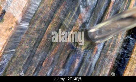 Der Wasserstrahl fließt aus einem blauen Swimmingpool auf eine Holzterrasse. Stockfoto