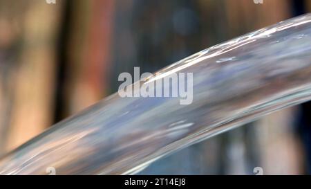 Der Wasserstrahl fließt aus einem blauen Swimmingpool auf eine Holzterrasse. Stockfoto