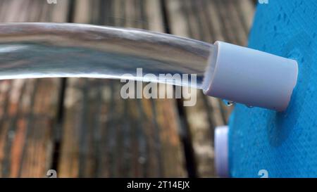 Der Wasserstrahl fließt aus einem blauen Swimmingpool auf eine Holzterrasse. Stockfoto