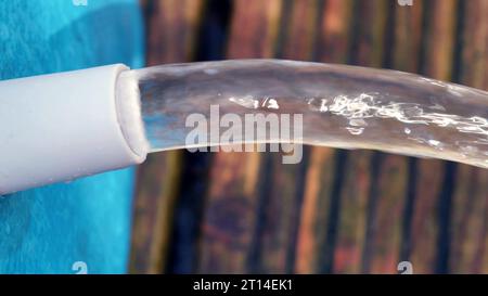 Der Wasserstrahl fließt aus einem blauen Swimmingpool auf eine Holzterrasse. Stockfoto