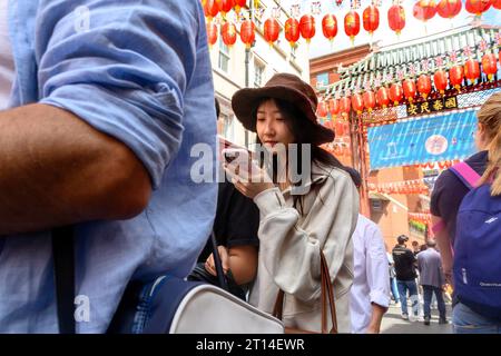 London, England, Großbritannien. Ein junges chinesisches Paar in Chinatown. Frau, die ihr Handy überprüft Stockfoto