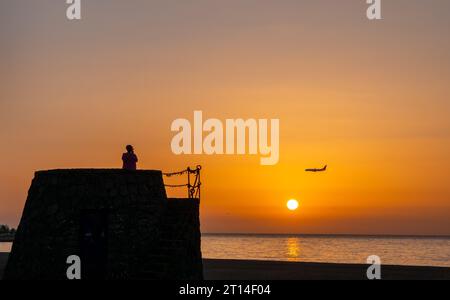 Lanzarotte, Spanien. Oktober 2023. REISE, Business, Tourismus, Puerto del Carmen, Lanzarote, Kanarische Inseln, Spanien. Ein Blick auf einen Touristen, der vom Strand von Puerto del Carmen auf Lanzarote aus sieht, während die Sonne aufgeht und ein Flugzeug sich auf die Landung am Flughafen Arrecife vorbereitet. Bildnachweis: phil wilkinson/Alamy Live News Stockfoto