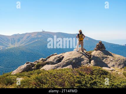 Frau, die die Landschaft neben einem Meilenstein bewundert, nach dem Aufstieg auf einen Berg ruht. Stockfoto