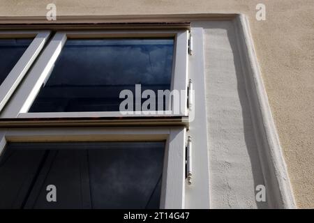 Fensterrahmen aus weiß lackiertem Holz in Stuck-Außenwand. Flachwinkelansicht. Altes Stahlscharnier. Dunkles Fenster. Gefleckte Textur. Perspektivische Ansicht Stockfoto
