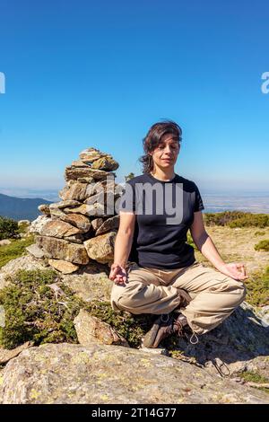 Frau, die neben einem Meilenstein sitzt, in leichter Position, mit ihren Händen in einer Chin Mudra-Position, für eine Meditationsübung inmitten der Natur. Stockfoto