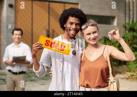 Porträt eines glücklichen, aufgeregten Paares mit verkauftem Schild und Schlüsseln aus dem neuen Haus Stockfoto