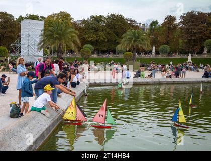 Ein Vater spielt mit seinen Kindern, während sie Modellsegelboote auf dem Teich im Herzen des beliebten Jardin du Luxembourg in Paris starten. Stockfoto