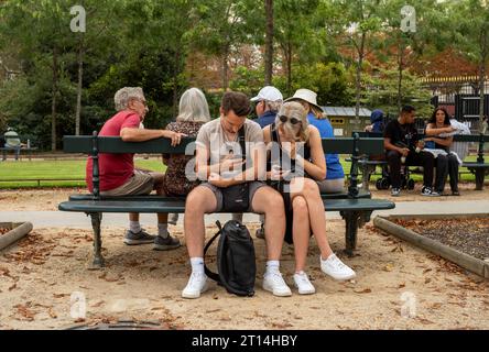 Ein Paar sieht sich Mobiltelefone an, während sie zusammen auf einer Parkbank im Jardin du Luxembourg in Paris sitzen. Stockfoto
