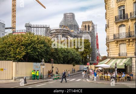 Die Menschen sitzen in Straßencafés hinter der Kathedrale Notre Dame in Paris, Frankreich, und zeigen die Kirche mit Gerüsten und einem großen Kran, während sie wieder aufgebaut wird Stockfoto