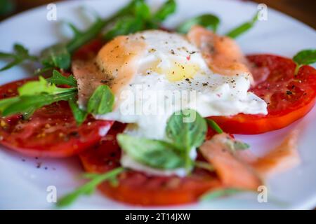 Gekochtes pochiertes Ei mit Kräutern, leicht gesalzenem Lachs und Tomaten mit Gewürzen auf einem Holztisch. Stockfoto