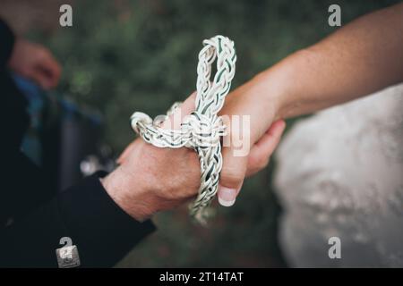 Nahaufnahme der Hände von Braut und Bräutigam, die mit weißem und grünem Seil gebunden sind. Stockfoto