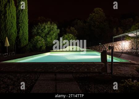 Beleuchteter Swimmingpool auf dem Hügel von Montemassi, umgeben von Zypressen und Oleandern in der Provinz Grosseto. Italien Stockfoto