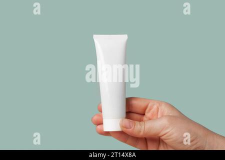 Weiße Creme-Verpackungsschablone in weiblicher Hand. Grüner Hintergrund. Naturkosmetik Zeigen. Mockup Für Schönheitsprodukte. Hautpflege, Gesichtsmaske, Toner. V vorn Stockfoto