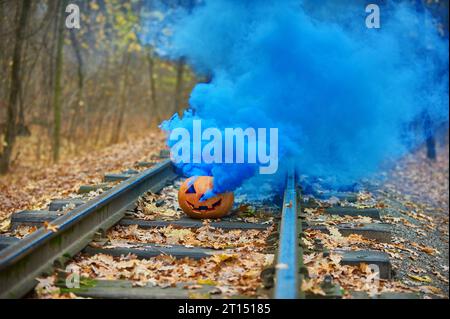 Lächelnder halloween-Kürbis mit hellblauem Rauch auf den Schienen im Wald. Selektiver Fokus. Stockfoto