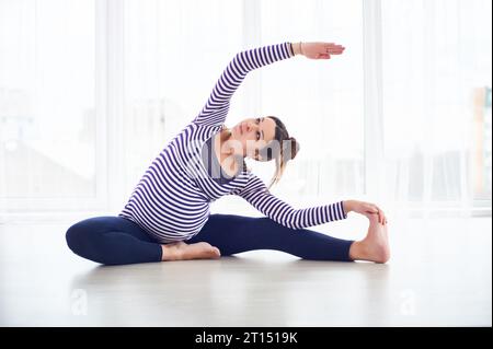 Junge schöne schwangere Frau macht Yoga Asana Parivrtta Janu Sirsasana zu Hause. studio-Aufnahme. Stockfoto