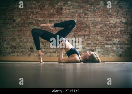 Schöne junge Frau übt Yoga Asana Sarvangasana im Yoga Studio auf einem Backsteinmauergrund. Stockfoto