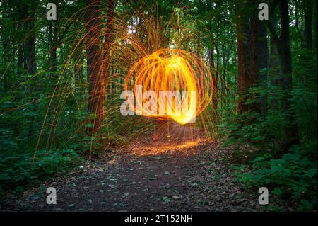 Brennende Stahlwolle, die sich im Wald verspinnt. Nächtliche Schauer von leuchtenden Funken aus spinnender Stahlwolle. Stockfoto