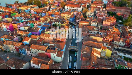 Blick aus der Vogelperspektive auf Burano farbenfrohe Häuser, entlang des Fondamenta Dammes, mit Fischerbooten und Brücken, Venedig, Italien bei Sonnenaufgang goldene Stunde Stockfoto