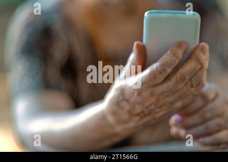 In der Natur greifen die Hände eines Älteren auf Holzdielen mit den komplexen Problemen eines Smartphones. Geräte werden für viele zu Barrieren, nicht zu Brücken Stockfoto