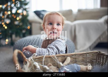 Porträt eines niedlichen 1-jährigen Jungen, der auf dem Boden sitzt. weihnachtsdekoration auf einem Hintergrund. Stockfoto