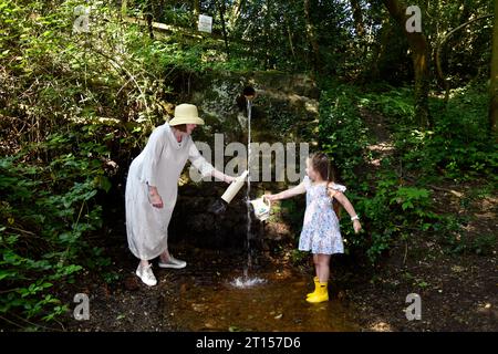 Frau und Kind sammeln frisches Quellwasser aus der Wasserleitung der Mine, angeblich reines Wasser, Spout Lane, Benthall, Shropshire Stockfoto