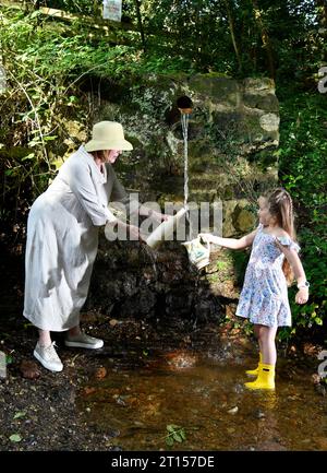 Frau und Kind sammeln frisches Quellwasser aus der Wasserleitung der Mine, angeblich reines Wasser, Spout Lane, Benthall, Shropshire Stockfoto