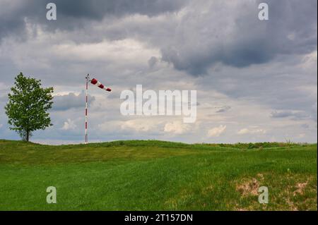 Windsocke, vom Wind geweht mit bewölktem Himmel, einsamem Baum und grünem Rasen. Stockfoto